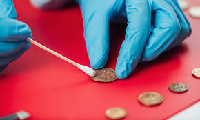 Técnica correcta de limpieza de monedas con guantes azules y herramienta de precisión
