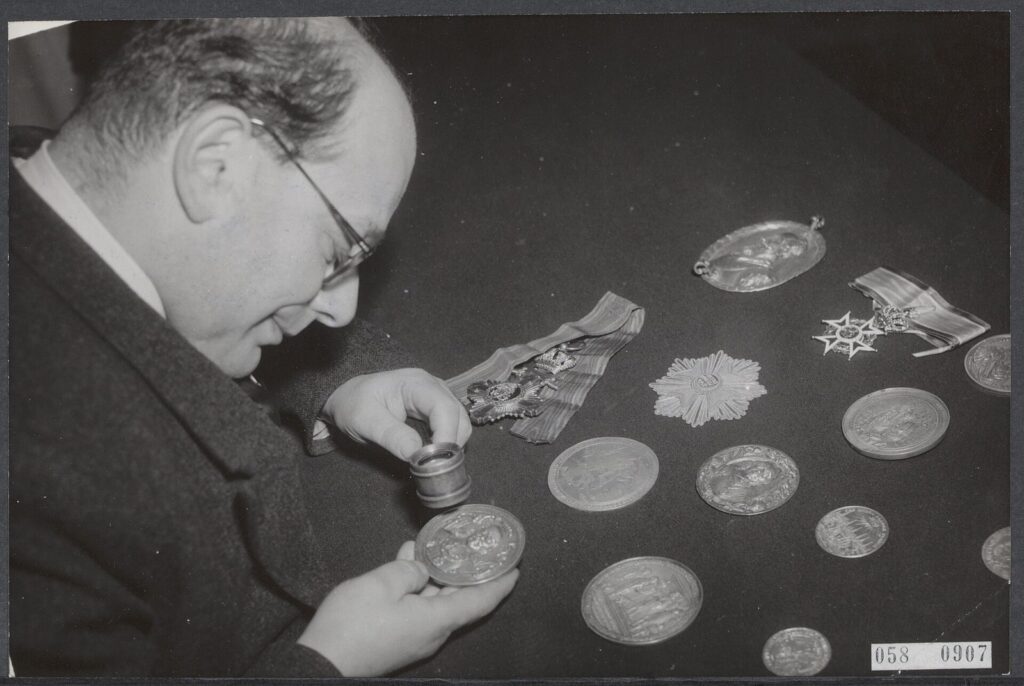 Numismático examinando monedas y medallas antes de una subasta en 1953