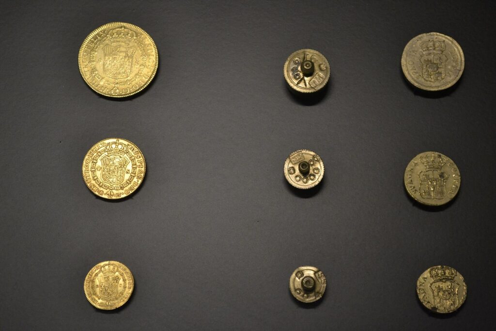 Monedas de oro de 8, 4 y 2 escudos del siglo XVIII junto a las pesas usadas para comprobar su peso